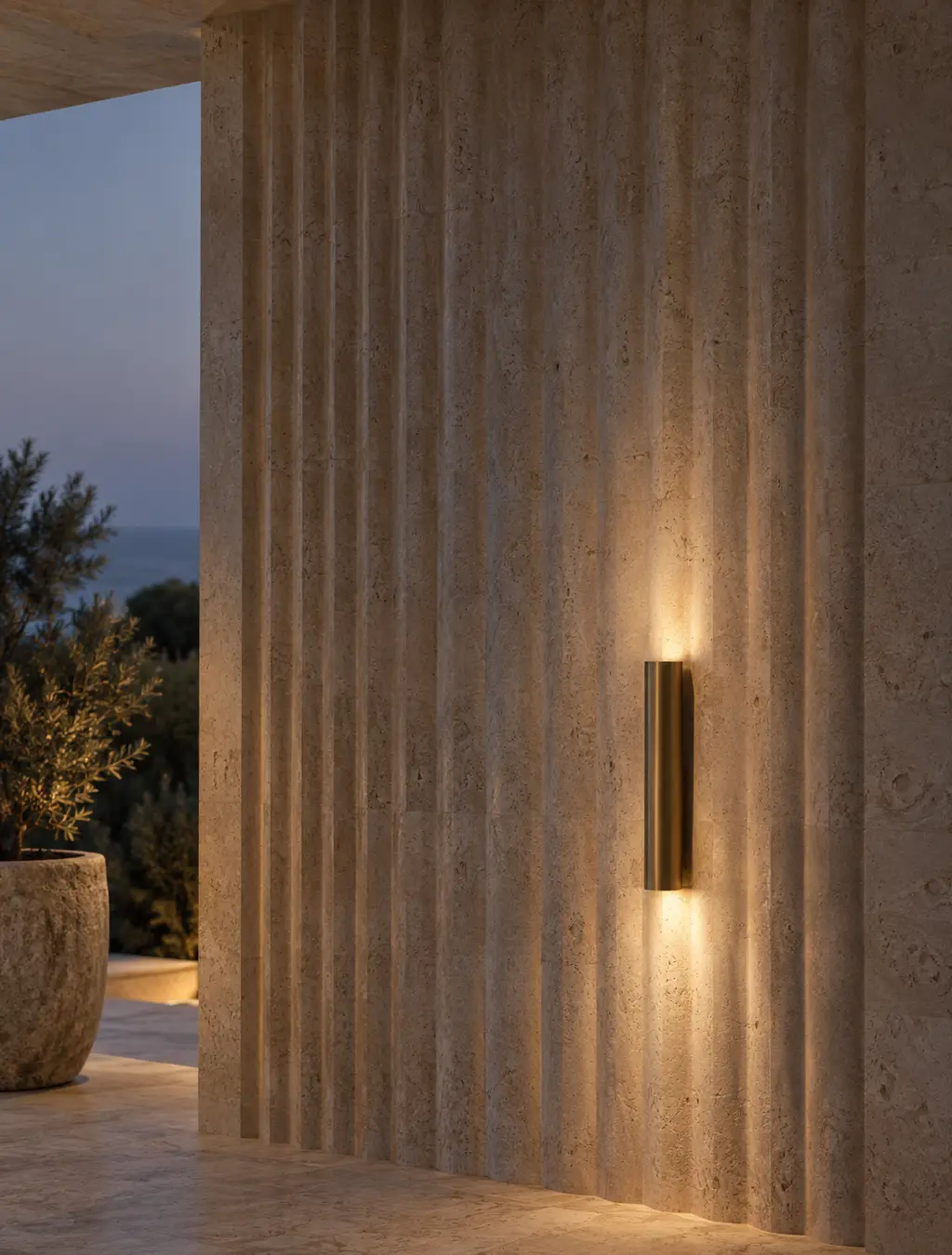 A fluted travertine wall with a brass sconce at dusk